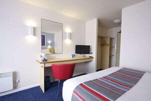Una habitación de hotel con una cama, un escritorio con ordenador, una silla y un armario.
