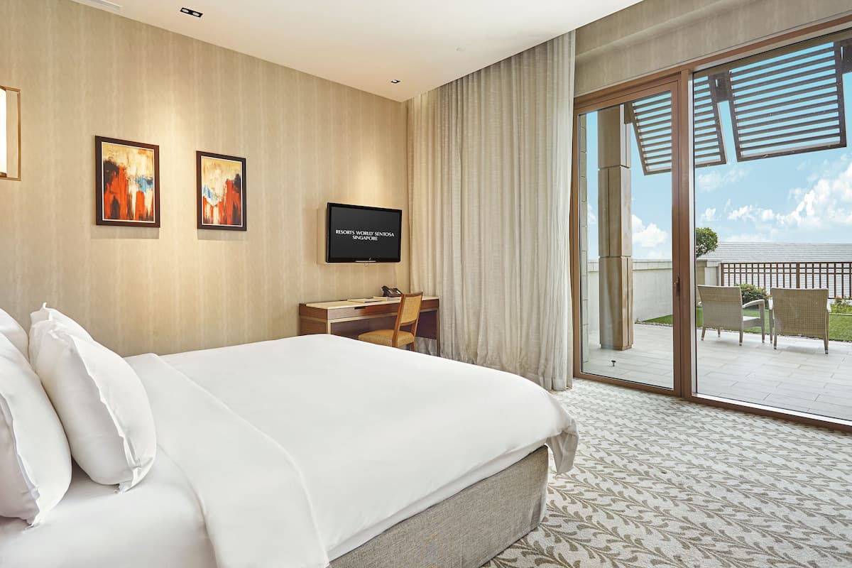 Une chambre d’hôtel avec un grand lit, un bureau, une chaise, une télévision et un balcon aménagé avec du mobilier d’extérieur.