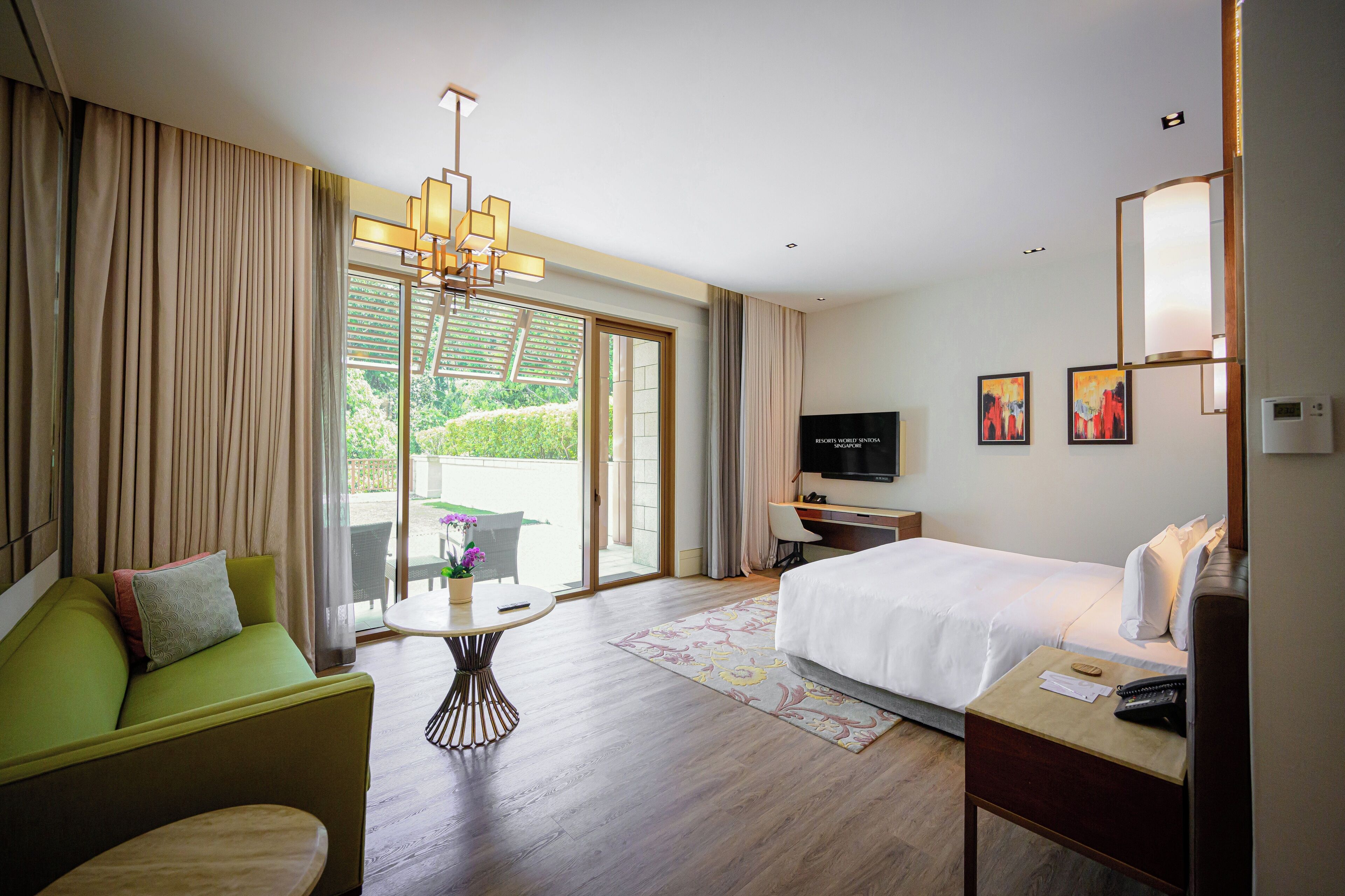 A hotel room with a bed, a sofa, a desk, a TV, and a balcony with curtains.