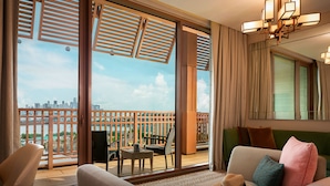 A hotel room with a balcony, a sofa, a dining table with chairs, and a view of the city skyline. - Resorts World Sentosa - Equarius Hotel (Singapore)