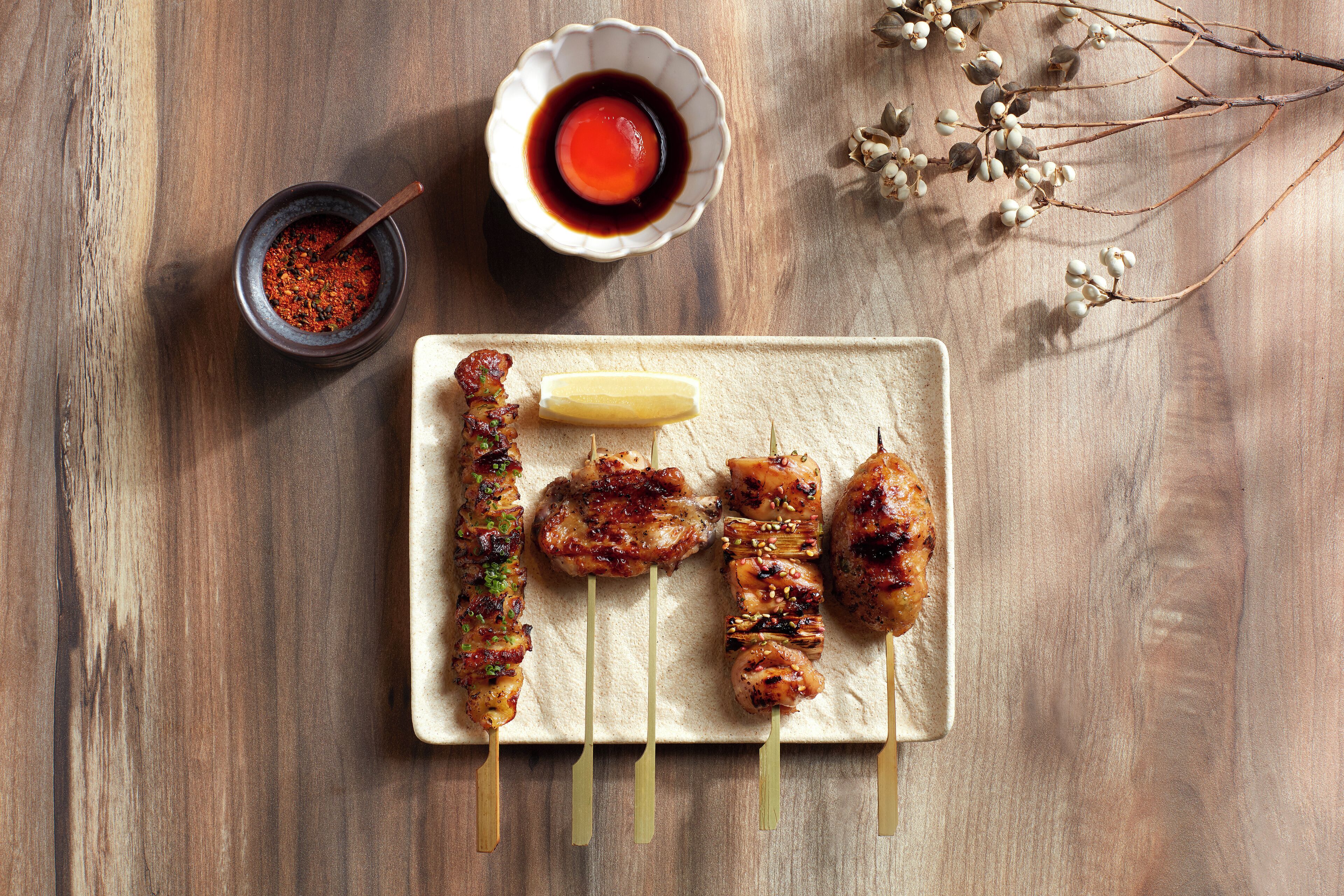 A wooden table with a plate of grilled skewers and a bowl of sauce.
