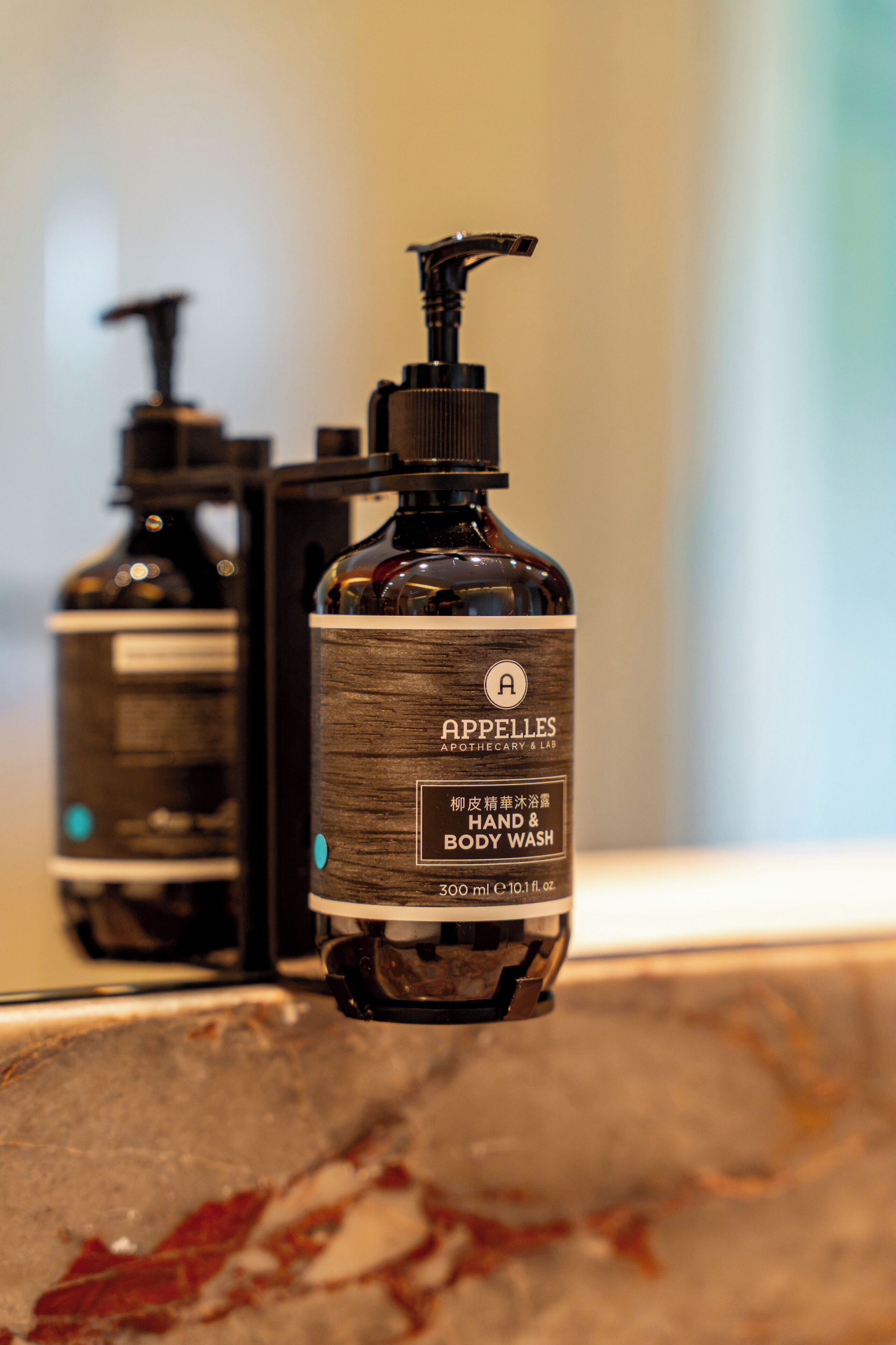 A bottle of hand and body wash with a pump dispenser, placed on a surface with a blurred background.