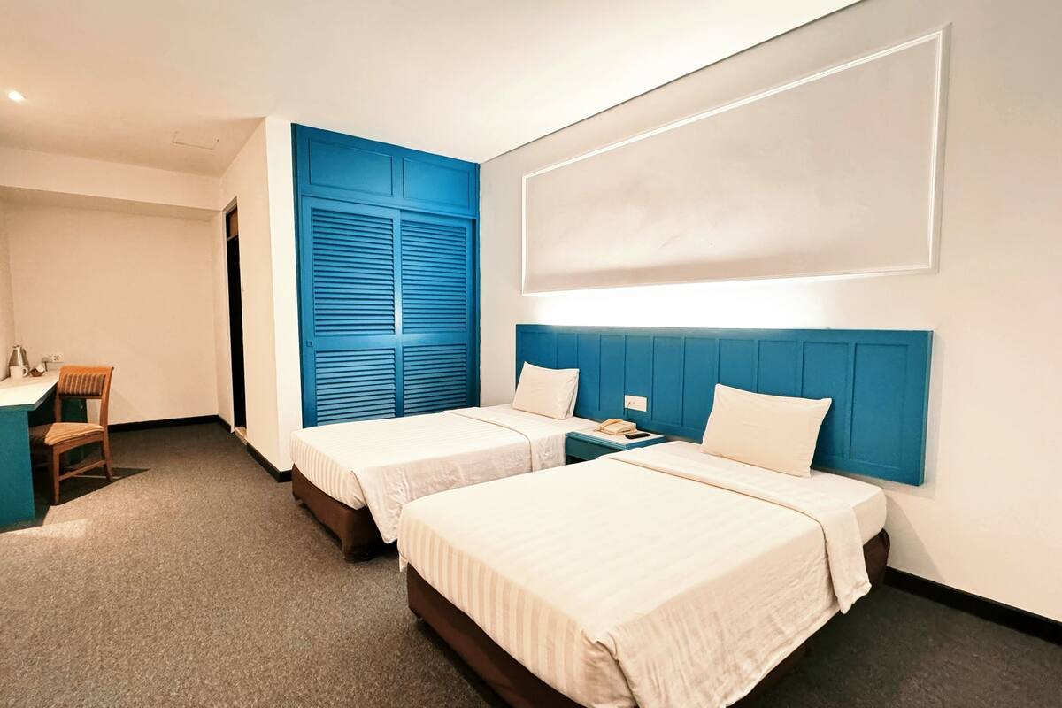 Habitación de hotel con dos camas, un escritorio, una silla y un ventanal grande.