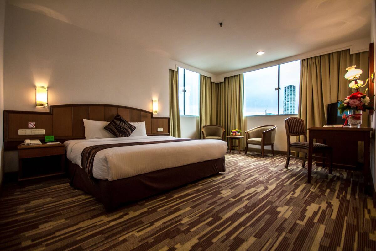Habitación de hotel con una cama grande, un escritorio, dos sillas, una mesita de noche y una ventana con cortinas.