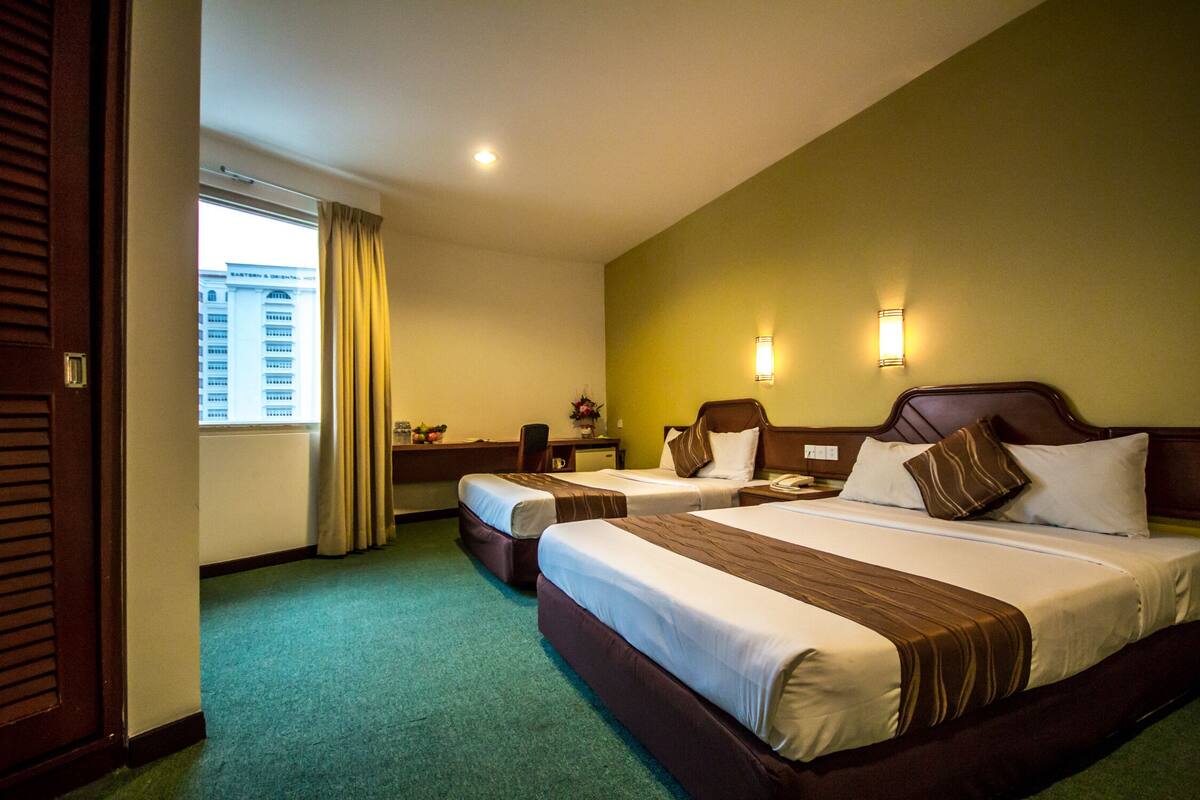 Habitación de hotel con dos camas, un escritorio, una silla y una ventana con cortinas.