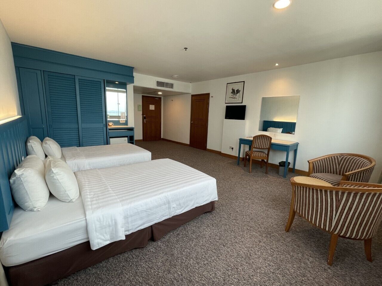 A hotel room with two beds, a desk, a chair, and a television.