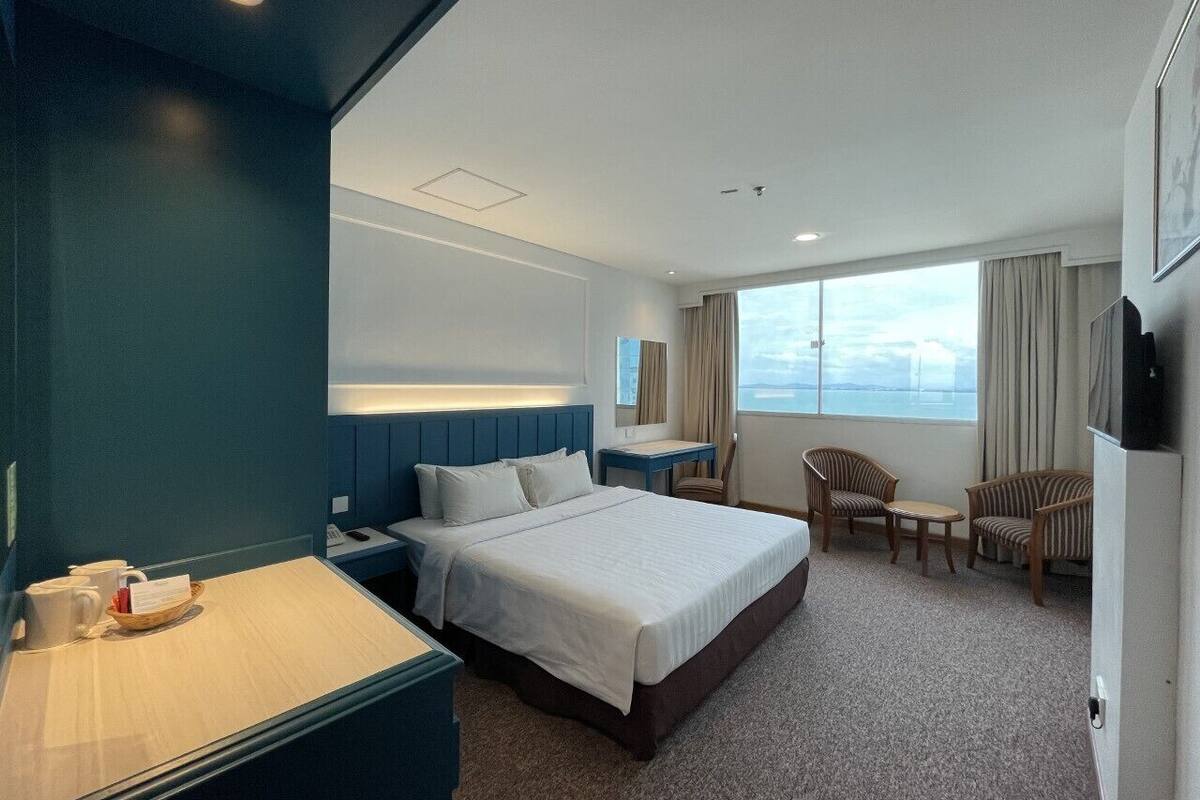 Habitación de hotel con una cama grande, un escritorio, dos sillas, un televisor y una ventana con vistas.