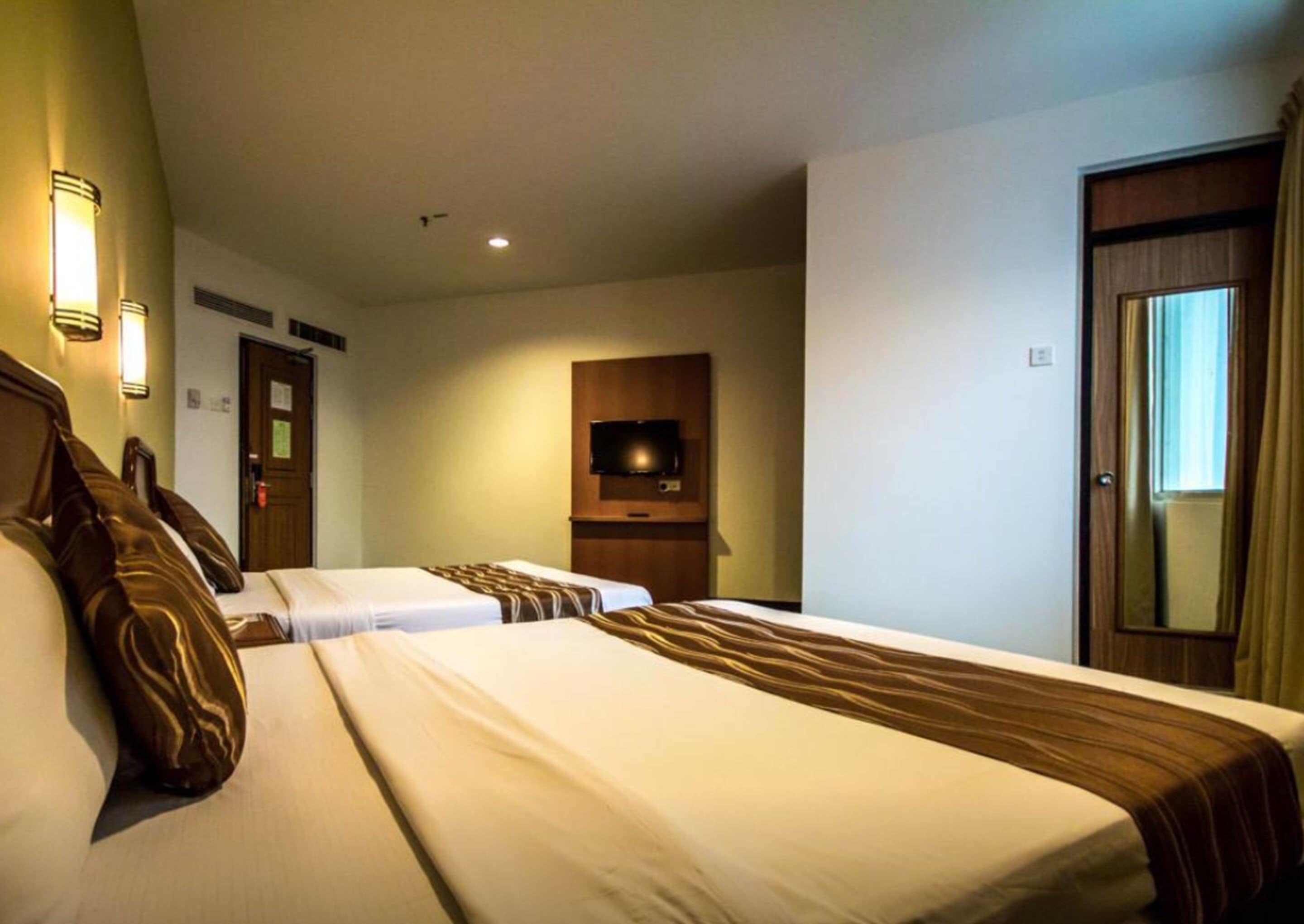 A hotel room with two beds, a television mounted on the wall, and a door with a mirror.