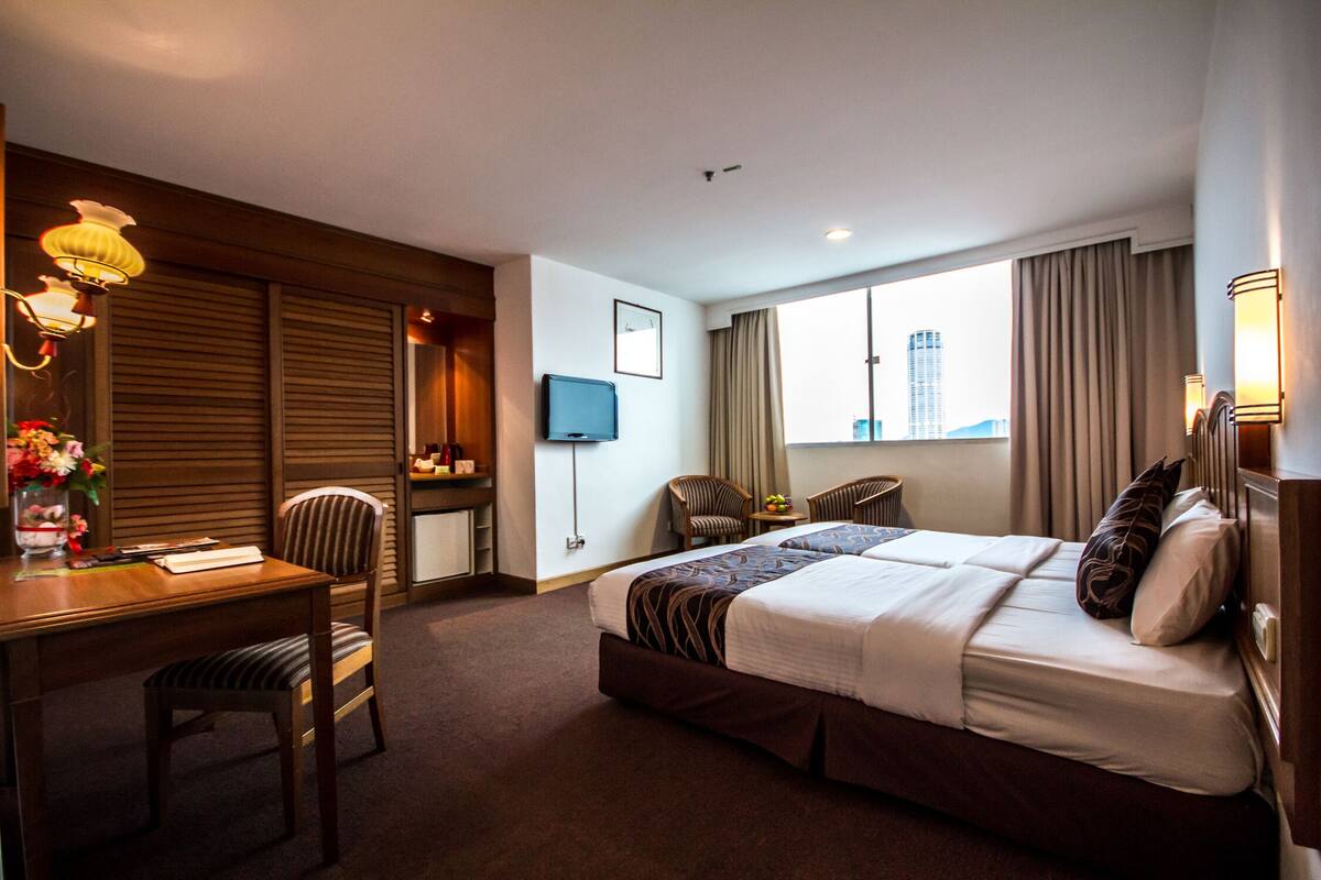 Habitación de hotel con una cama grande, un escritorio con silla, un televisor y una ventana con cortinas.