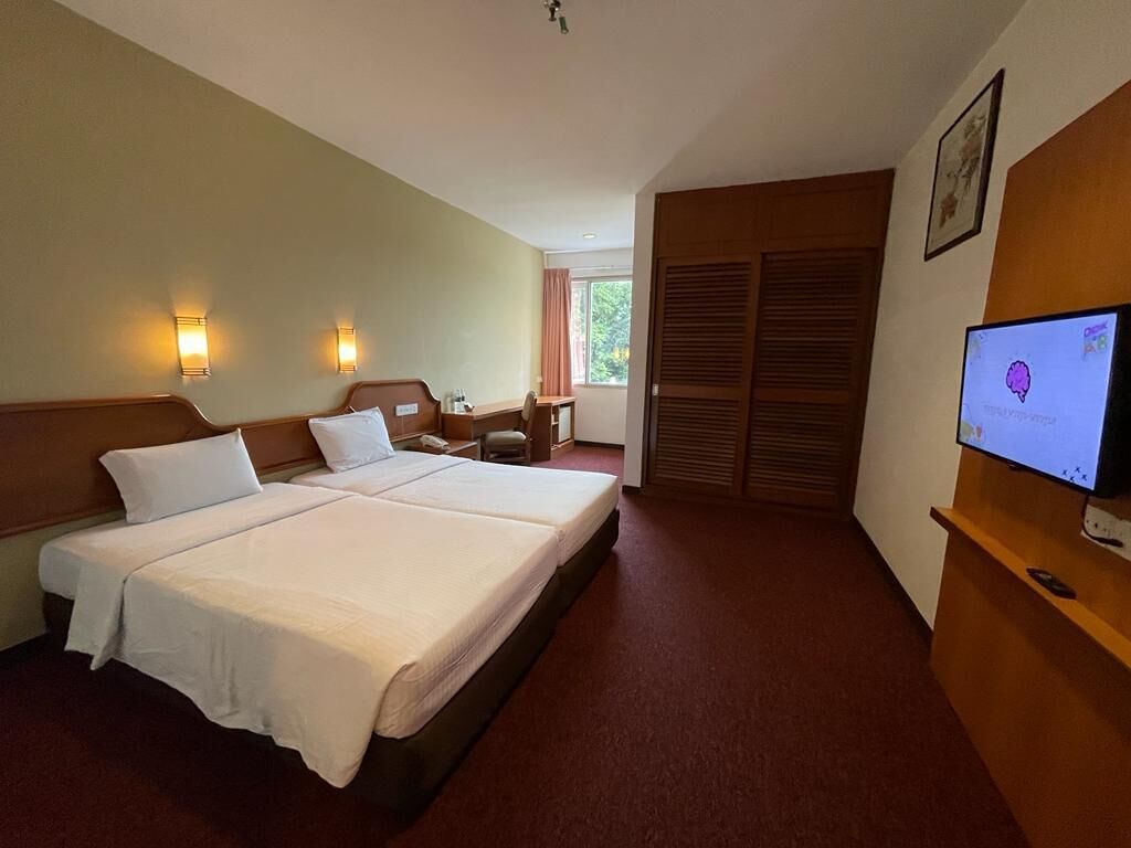 A hotel room with two beds, a desk, a chair, a TV, and a wardrobe.