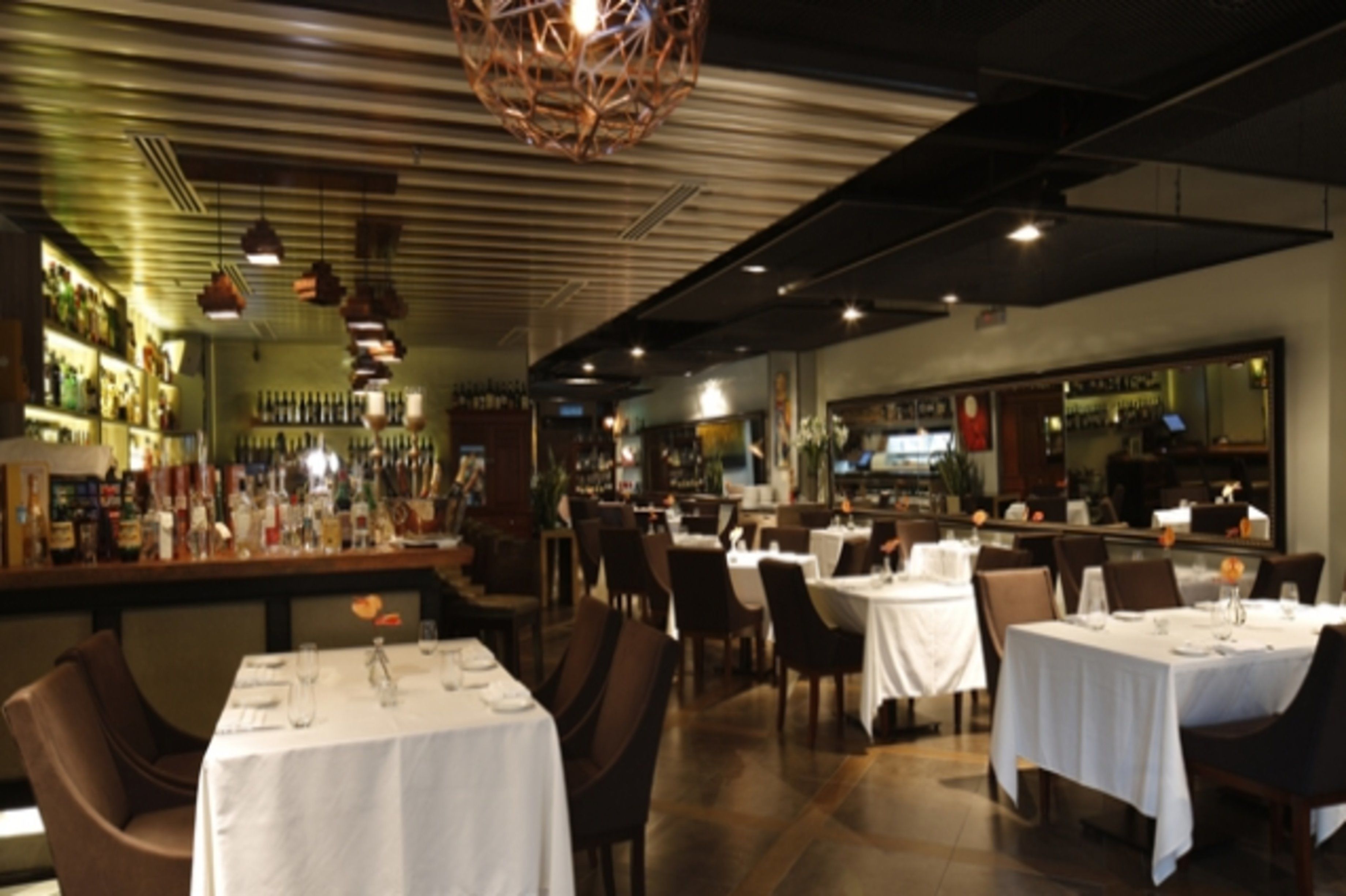 A restaurant with tables set for dining, a bar area with bottles, and a modern interior design.