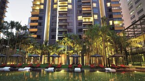 A high-rise hotel with multiple balconies, a swimming pool area with lounge chairs, and palm trees. - E&O Residences Kuala Lumpur (Kuala Lumpur)