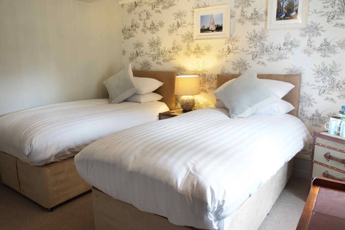 Habitación con cama doble y dos camas individuales, una mesita de noche con lámpara y un aparador con espejo.