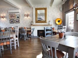 Un comedor con mesa y sillas de madera, chimenea y obras de arte colgadas en la pared.