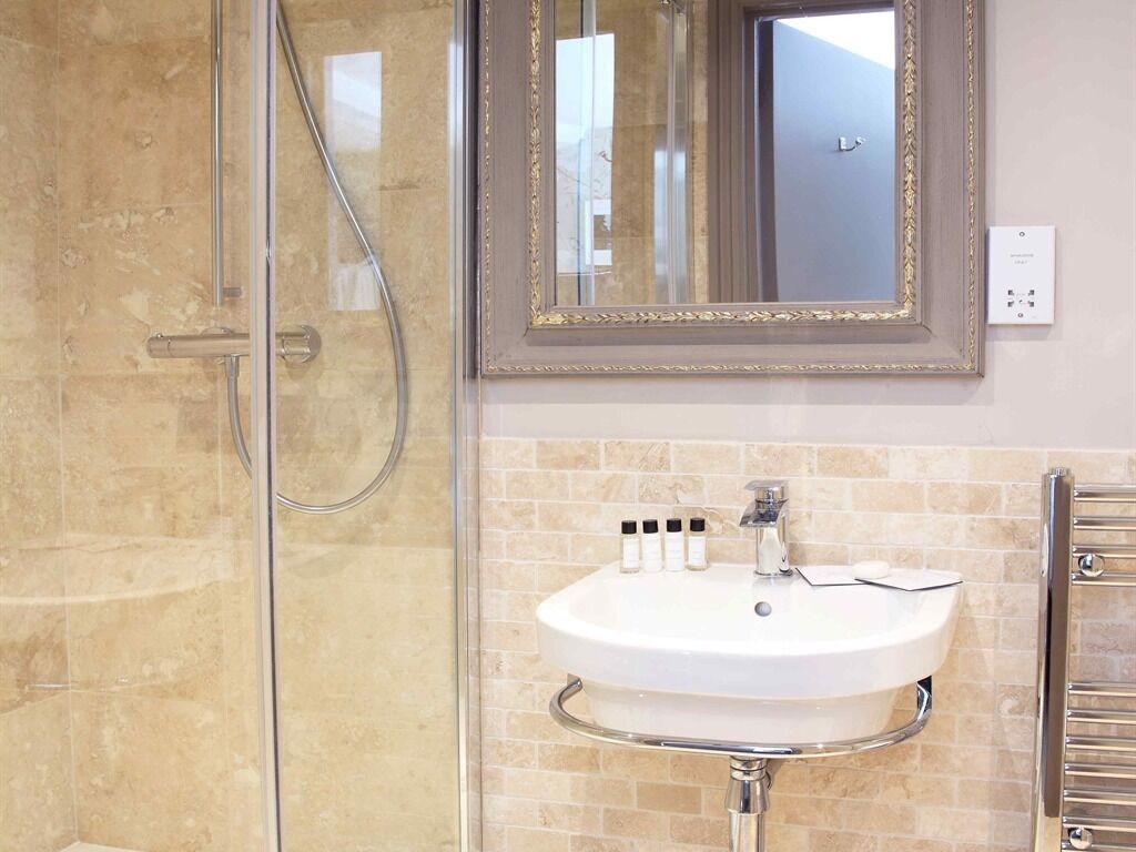A bathroom with a glass shower enclosure, a white sink with chrome fixtures, and a mirror with a gold frame.