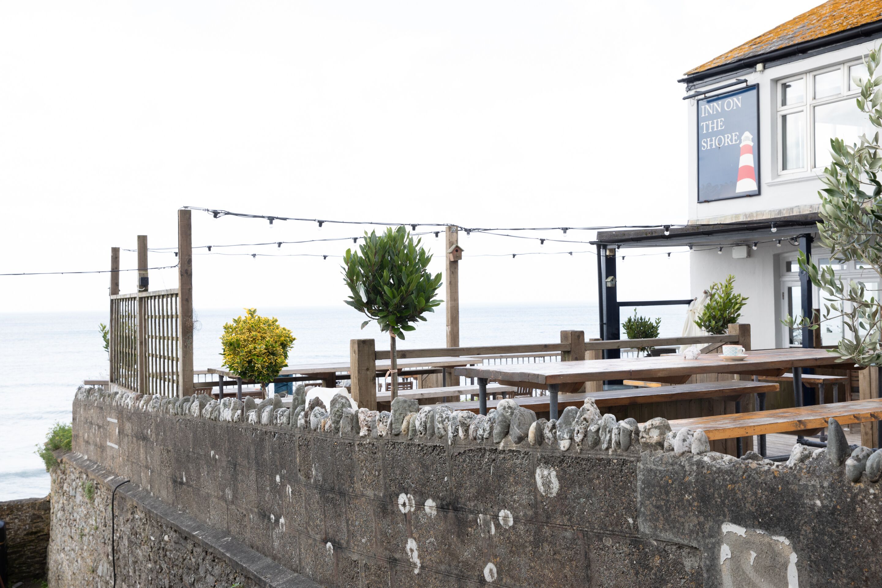 A seaside restaurant with outdoor seating, a stone wall, and a sign reading "Inn on the Shore".