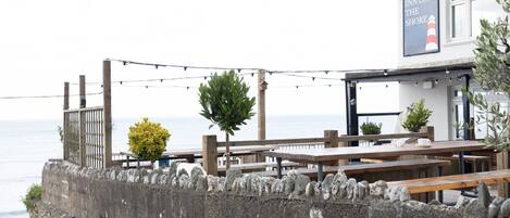 A seaside restaurant with outdoor seating, a stone wall, and a sign reading "Inn on the Shore".