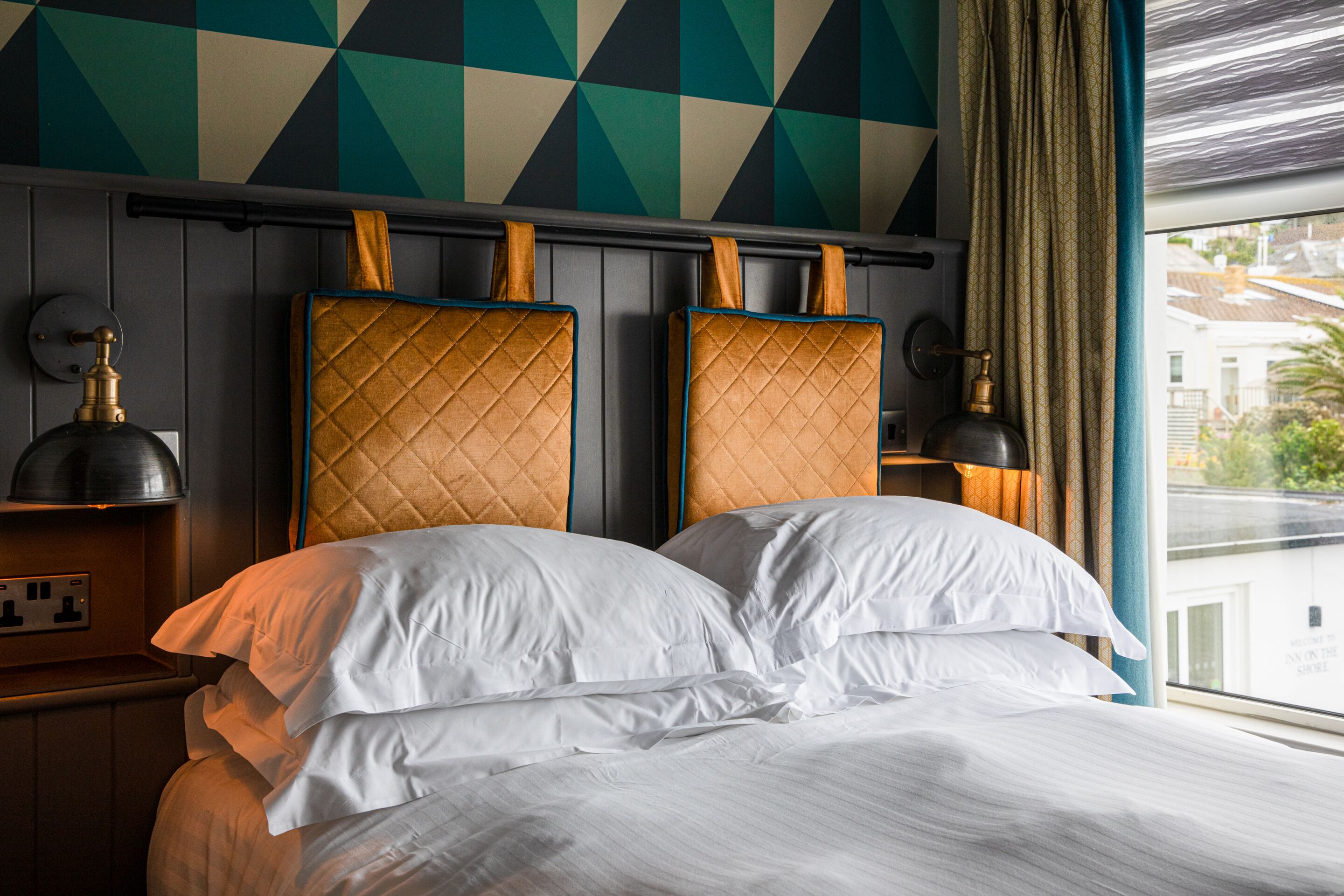 Una cama con dos almohadas, un cabecero con diseño acolchado y una pared de patrón geométrico.
