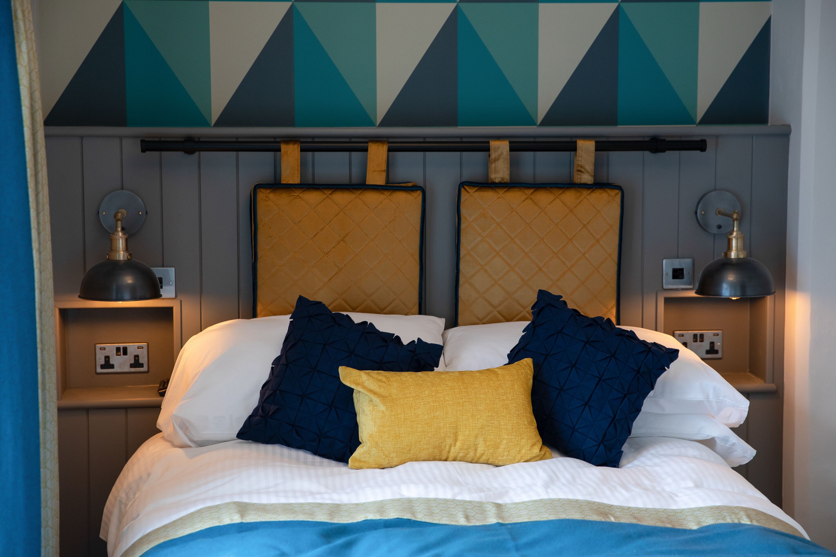A bed with a headboard, two bedside lamps, and a power outlet on the nightstand.