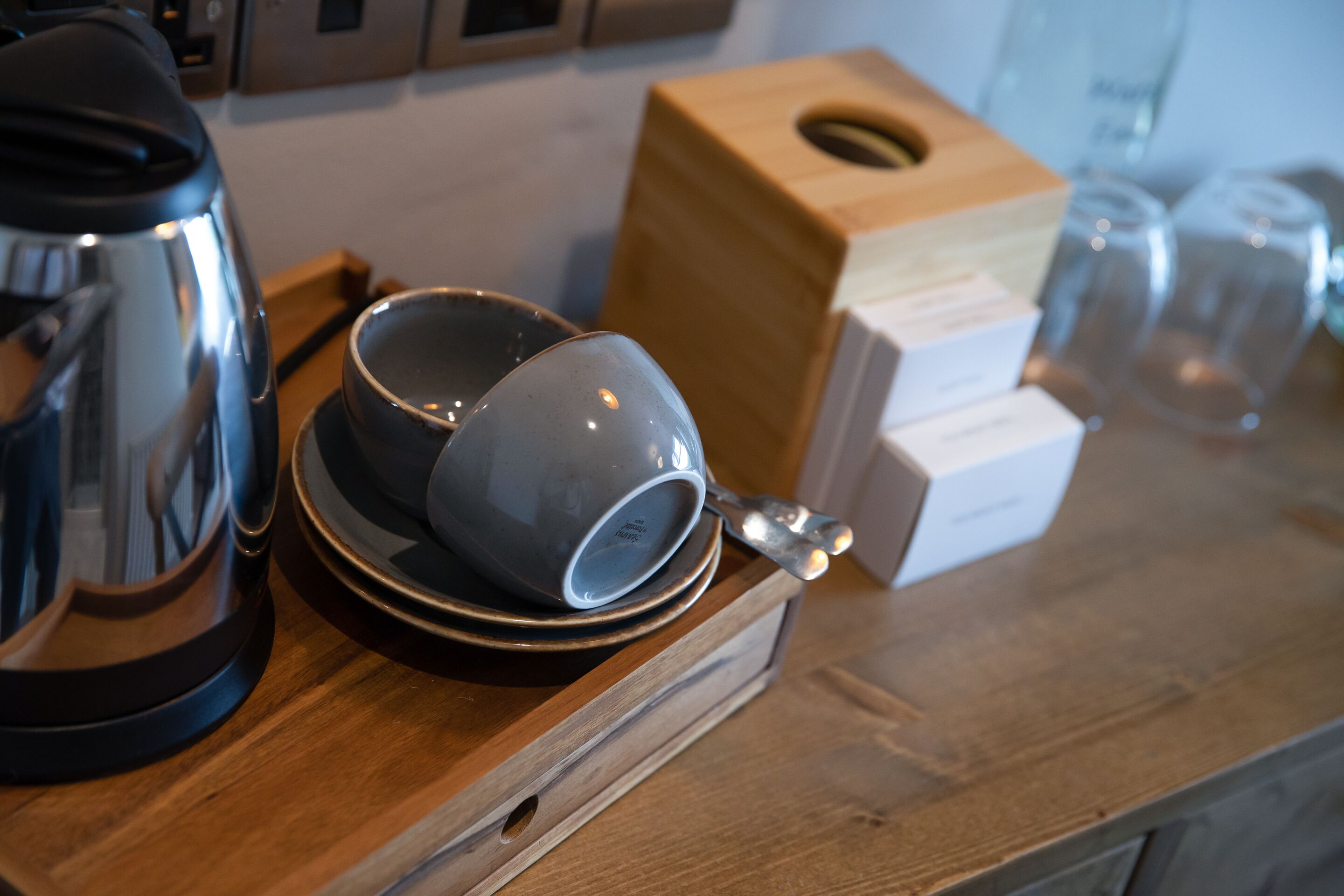Una encimera de madera con una cafetera, dos tazas, una caja y una cuchara.