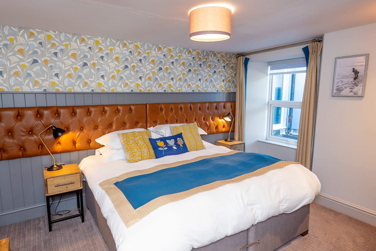 A neatly made bed with a blue and beige bedspread, a brown headboard, and decorative pillows.