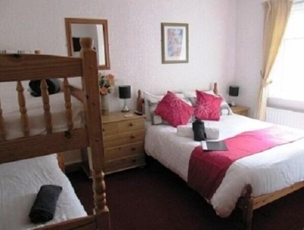 A bedroom with a wooden bed frame, white bedding, and pink pillows. There is a bedside table with a lamp, a mirror on the wall, and a framed picture above the bed.