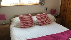 A neatly made bed with a white and pink striped pillow set, a pink blanket, and a wooden wardrobe to the right. - The Kingscliff (Blackpool)