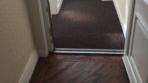 A hallway with a carpeted entrance, a door with a window, and a small bag on the floor. - The Kingscliff (Blackpool)