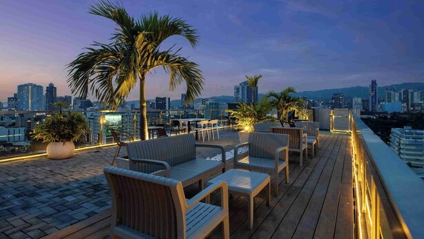 Terraza en la azotea con mobiliario, plantas en macetas y vista al horizonte urbano al anochecer.