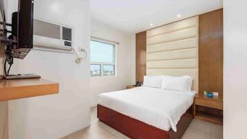 A bedroom with a bed, a bedside table, a nightstand, a TV mounted on the wall, and a window.