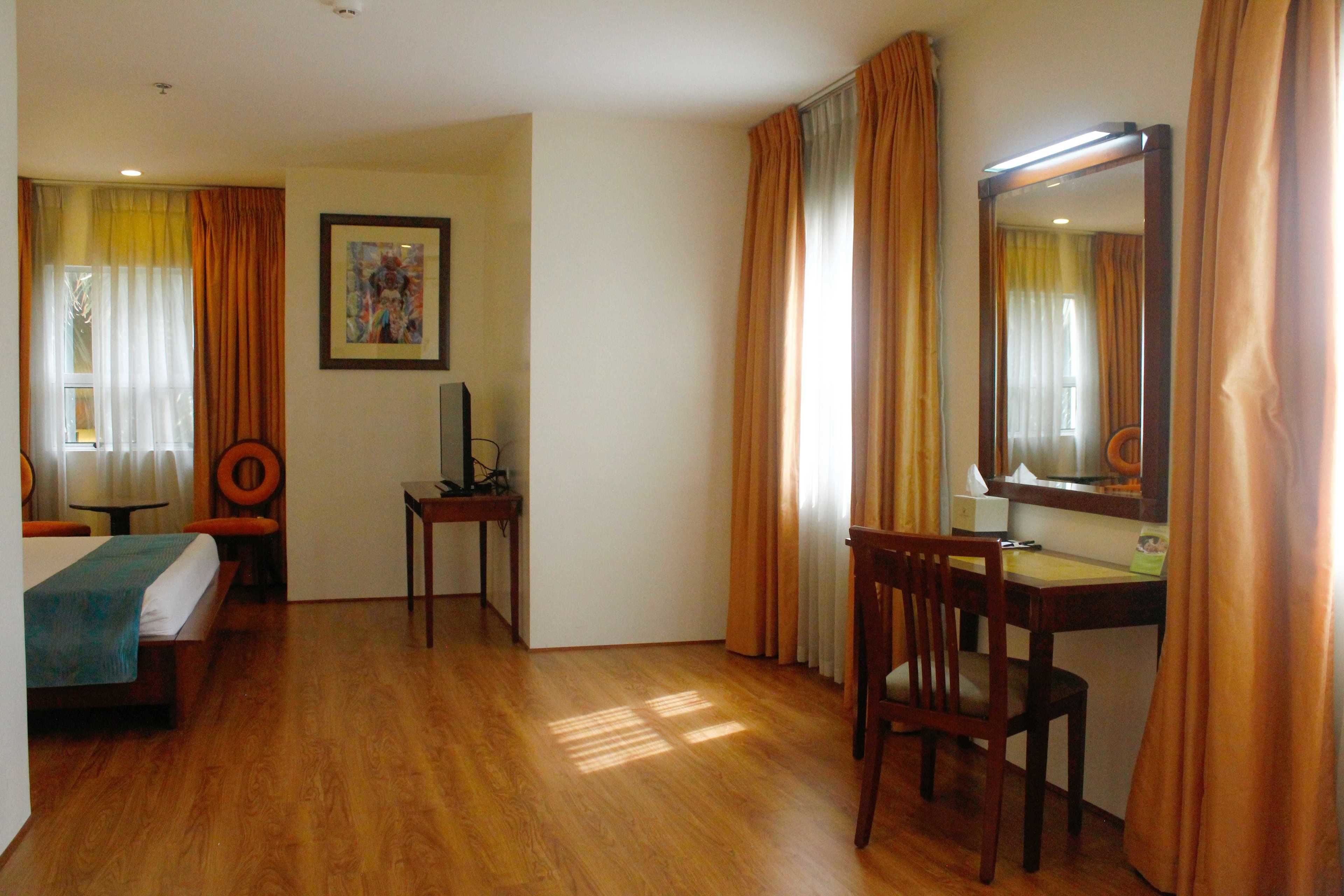 Una habitación de hotel con cama, escritorio, silla, espejo y un cuadro en la pared.