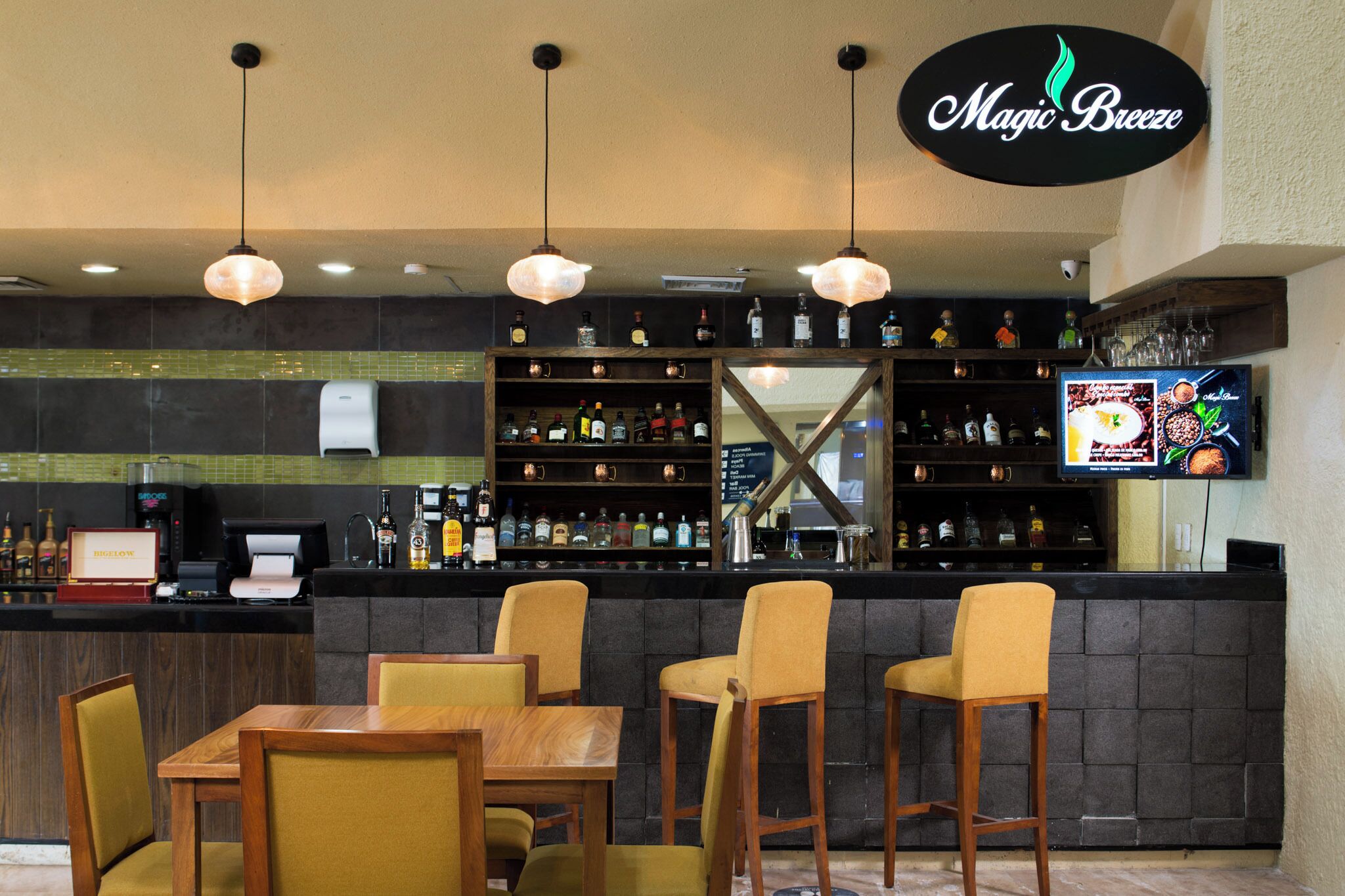 A bar area with a counter, multiple liquor bottles, a coffee machine, and a television screen displaying a menu.