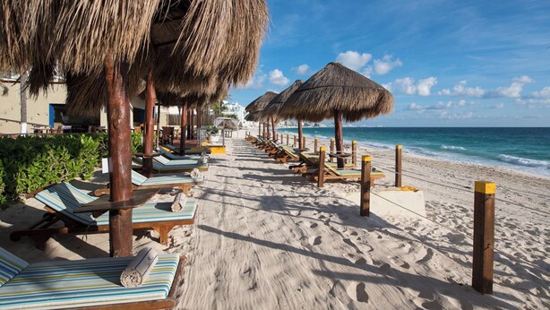 Een strand met rieten parasols, ligstoelen en een helder uitzicht op de oceaan.