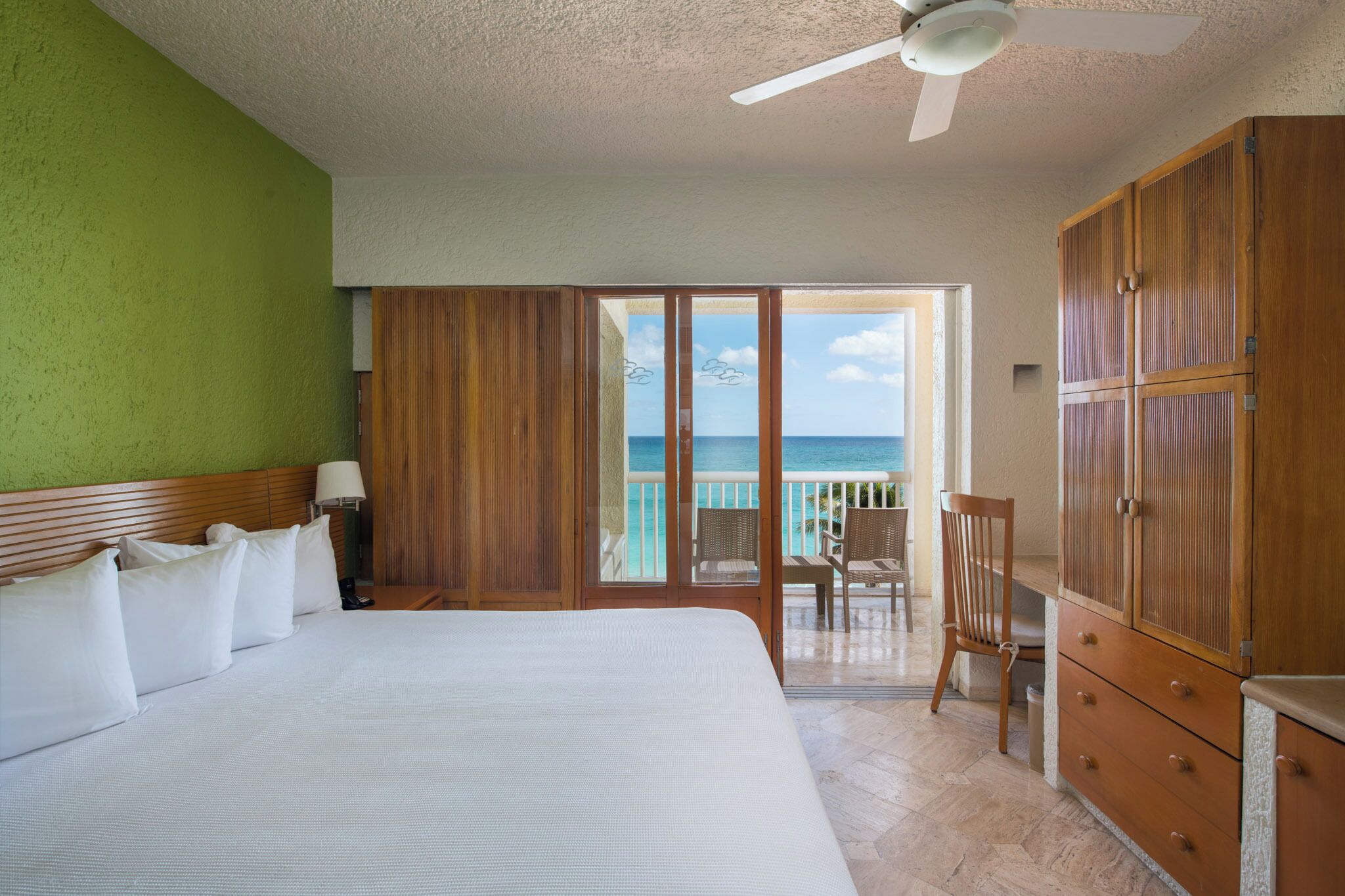 Habitación de hotel con cama, armario de madera, un escritorio y vista al océano.