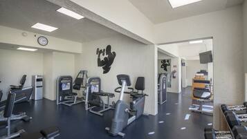 A gym with various exercise equipment, a clock, and a television on the wall.