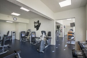 Un gimnasio con diversos equipos de ejercicio, un reloj y una televisión en la pared.