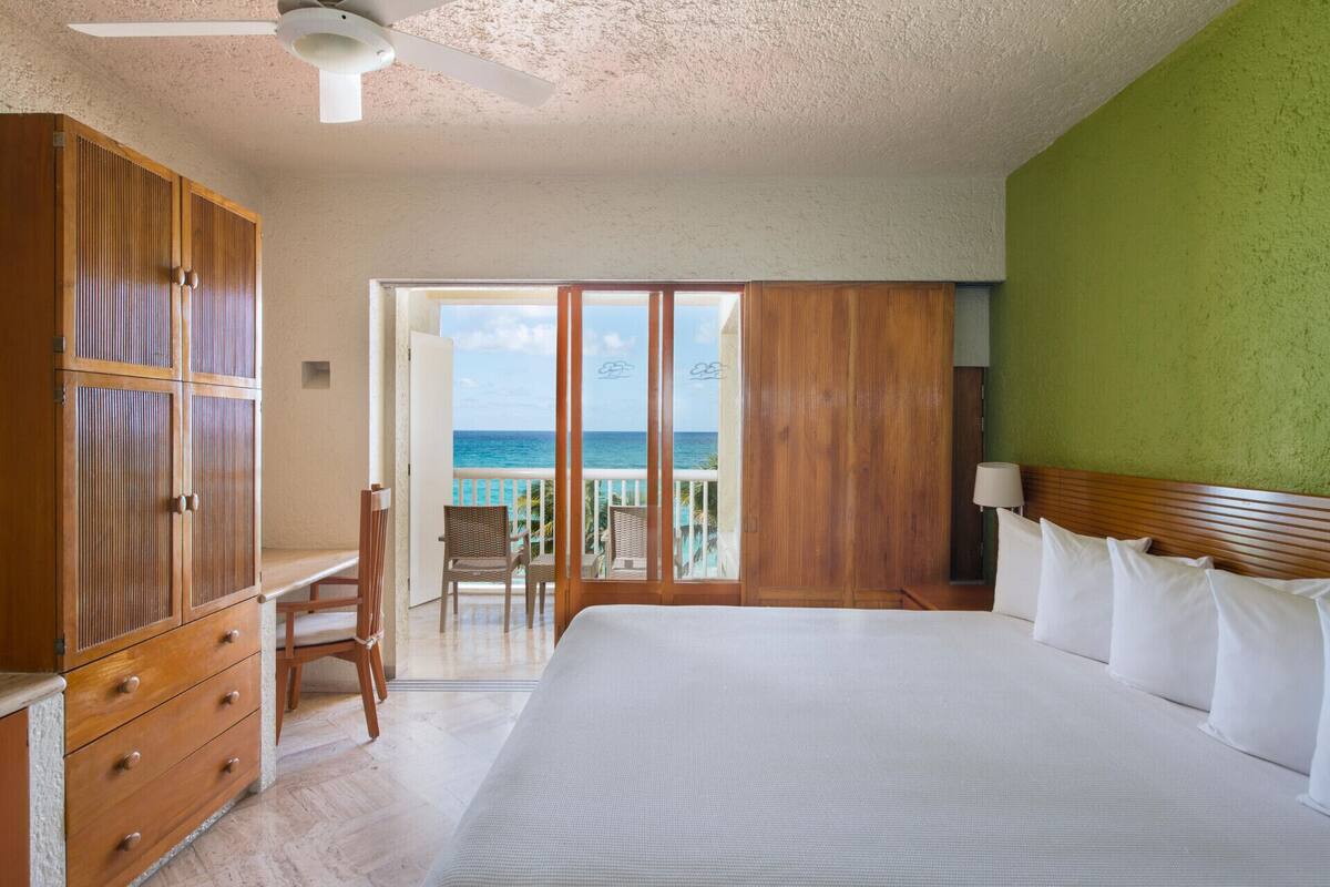 Habitación de hotel con una cama grande, armario de madera, un escritorio y vista al océano.