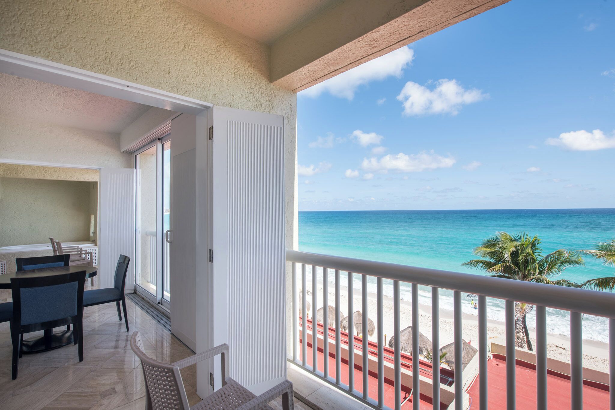 A balcony with a view of the ocean, a dining area with chairs and a table, and a sliding glass door.
