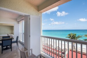 A balcony with a view of the ocean, a dining area with chairs and a table, and a sliding glass door.