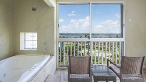 Een balkon met uitzicht op zee, een badkuip, rieten stoelen en een klein raam.
