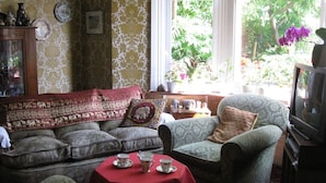Una sala de estar acogedora con un sofá, sillones, una mesita con tazas de té y un televisor.
