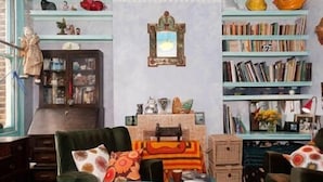 Una habitación acogedora con un sofá verde, un aparador de madera y una estantería llena de libros y objetos decorativos.