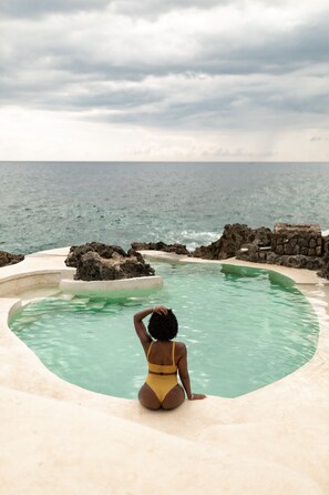 A person sitting by a curved pool with a view of the ocean and rocky formations. - Tingalaya's Retreat (Negril)