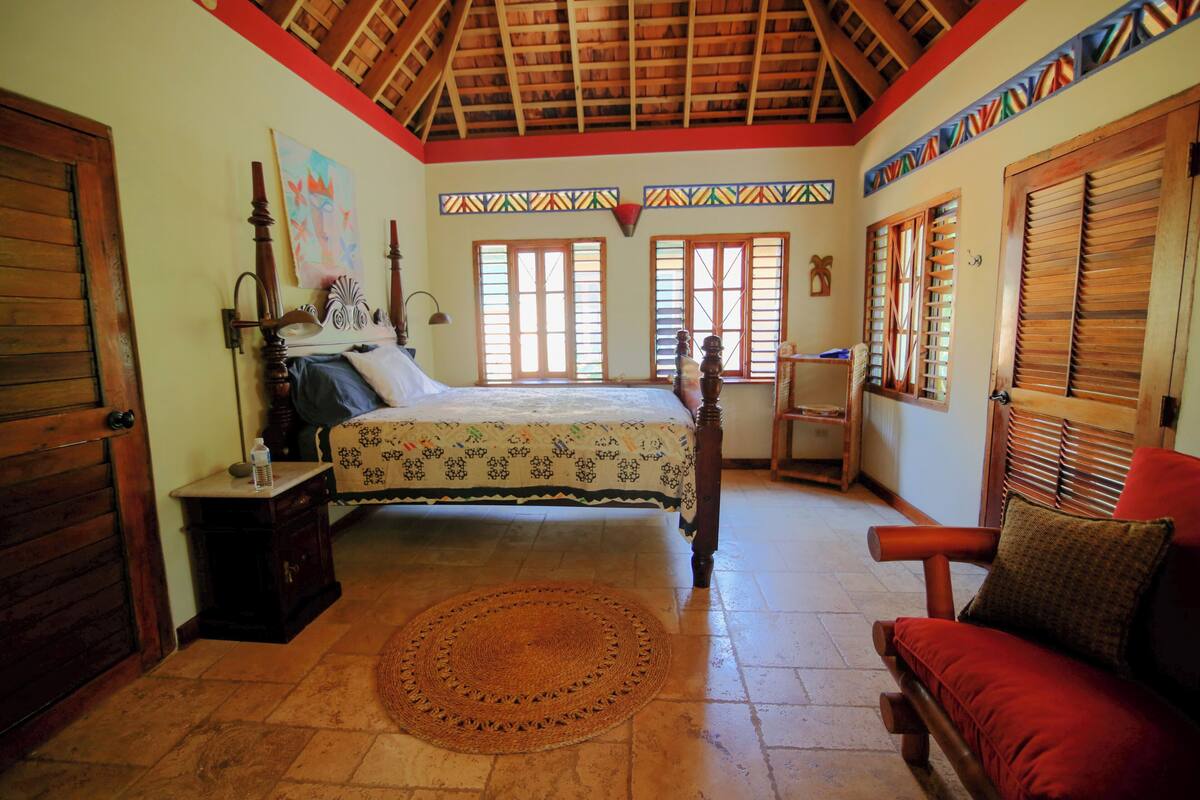 A bedroom with a bed, a nightstand, a chair, a window, and a door.