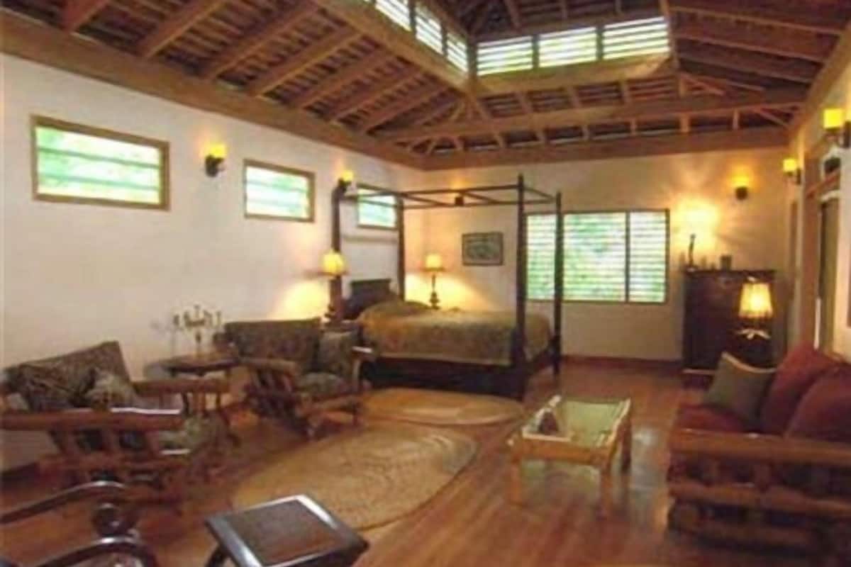 A room with a four-poster bed, wooden furniture, and large windows.