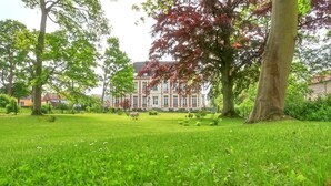 Une zone verdoyante bien entretenue, avec de grands arbres et un grand bâtiment en arrière-plan.