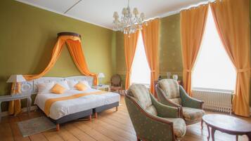 A room with a bed, two chairs, a table, a lamp, and a chandelier.