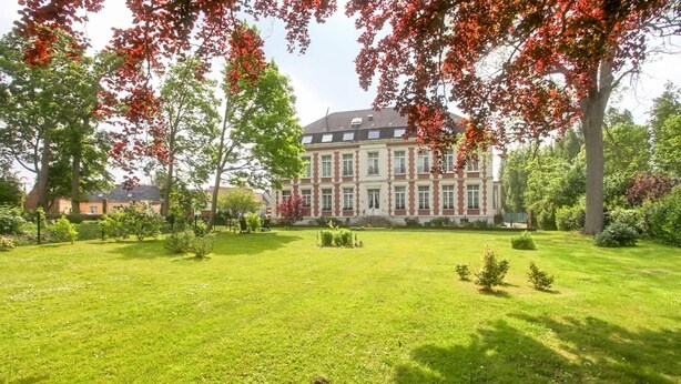 Un grand bâtiment historique à la façade symétrique, entouré d’une pelouse bien entretenue et d’arbres majestueux.