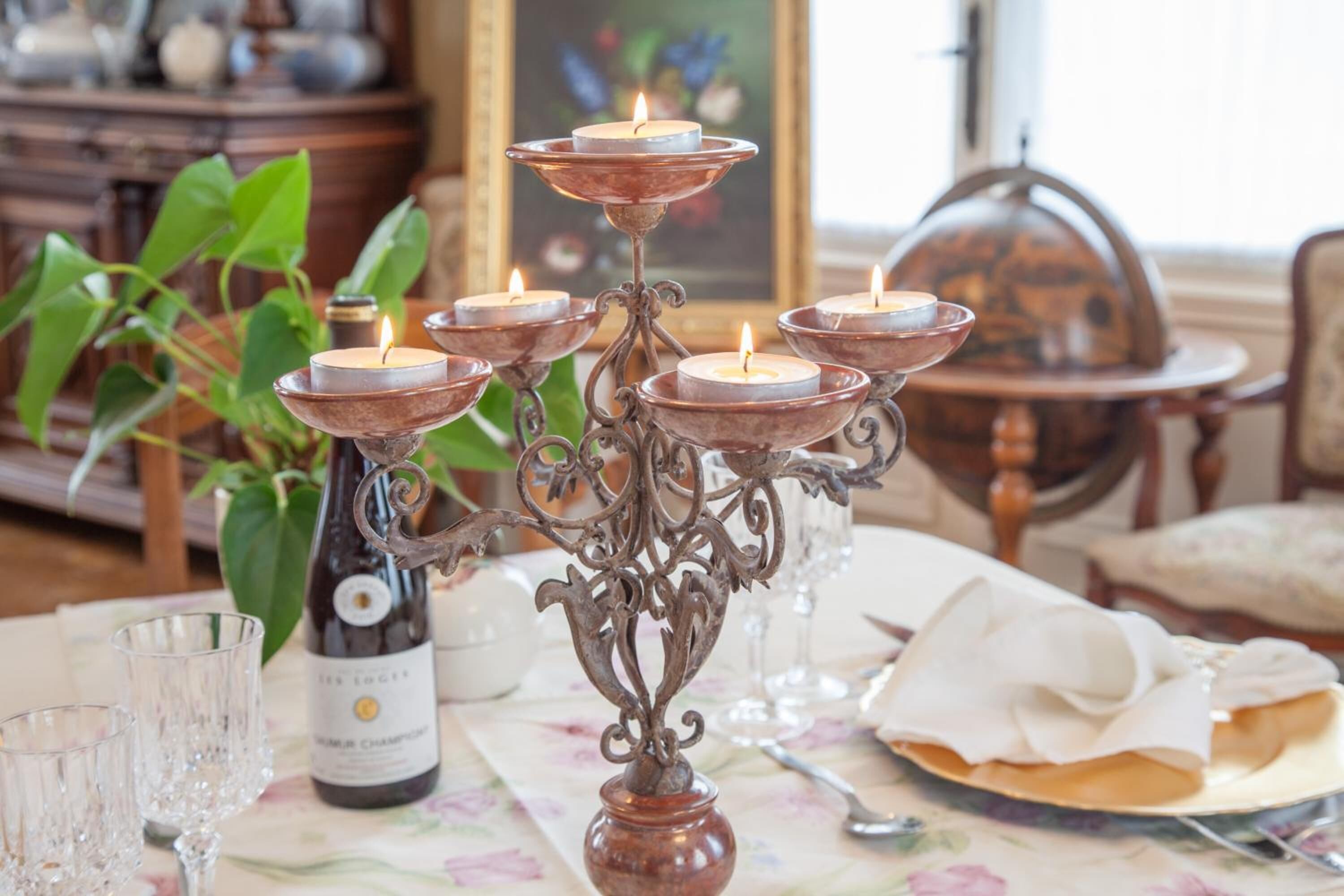 A dining table with a floral tablecloth, a bottle of wine, and a decorative candle holder with lit candles.