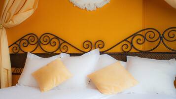 A bed with white linens and yellow pillows, a black metal headboard, and a yellow wall with a decorative white ceiling piece.